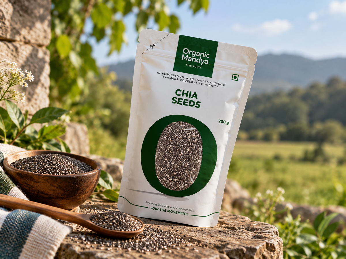 Organic Mandya Chia Seeds pouch on a stone ledge beside a wooden bowl and spoon of chia seeds, with a green field and hills behind