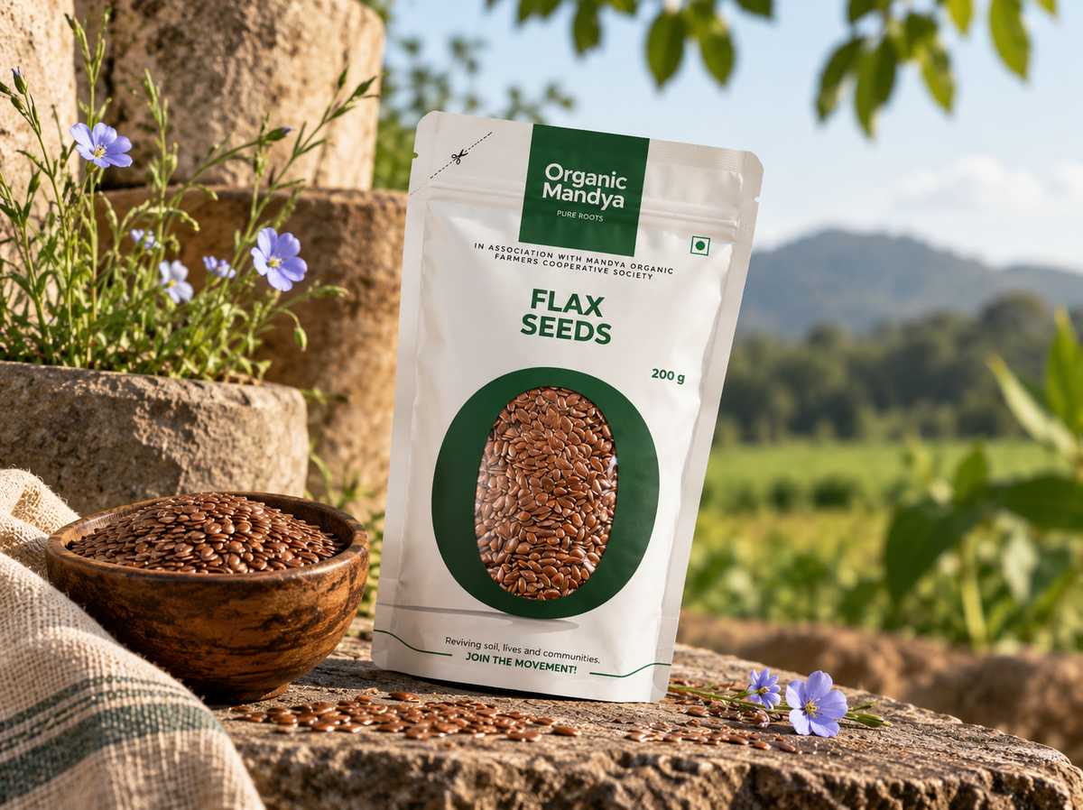 Organic Mandya Flax Seeds pouch on a stone ledge beside a wooden bowl of flax seeds, with blue flax flowers and a green field behind